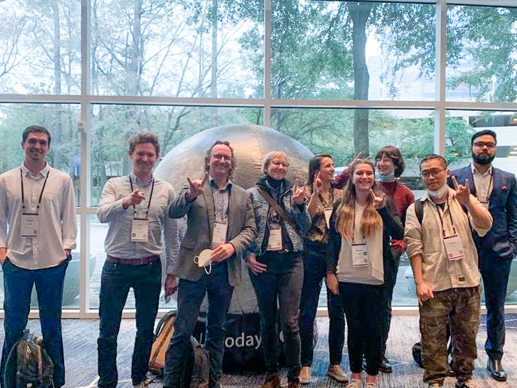 A group of nine people pose in front of a globe sculpture.