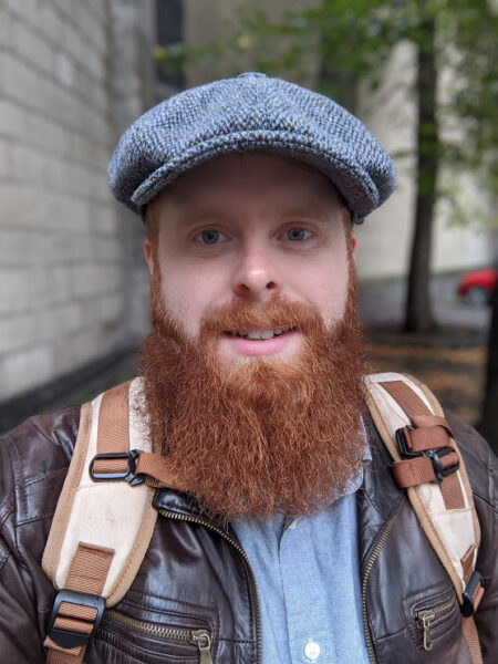 Photo of Brandt wearing a flat cap and sporting a full beard.